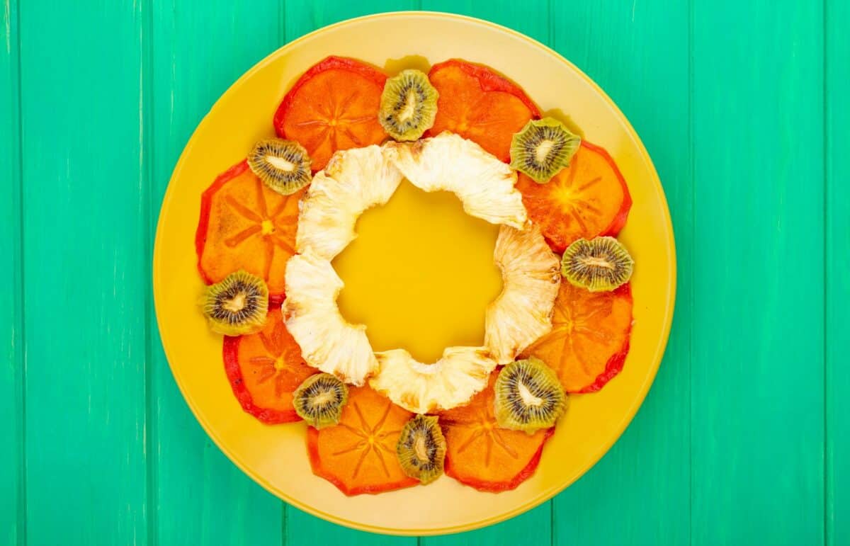 top view of dried persimmon slices with pineapple and kiwi slices arranged on a yellow plate