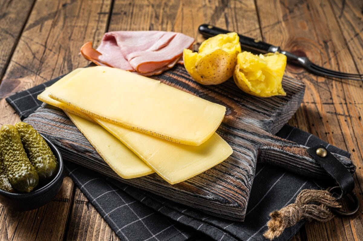 Tranches de fromage suisse à raclette prêtes à être cuisinées avec des pommes de terre bouillies et du jambon.