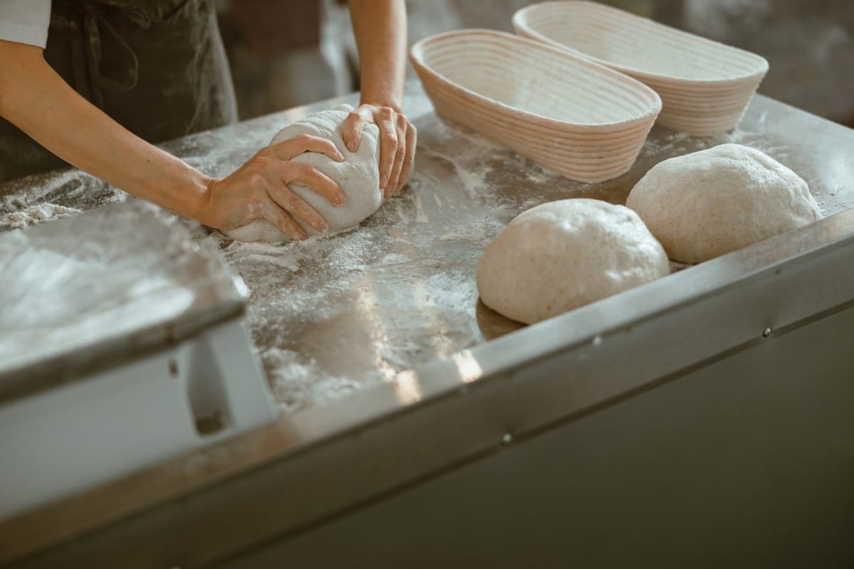 Un ouvrier pétrit la pâte à pain sur une table métallique dans une boulangerie artisanale moderne.