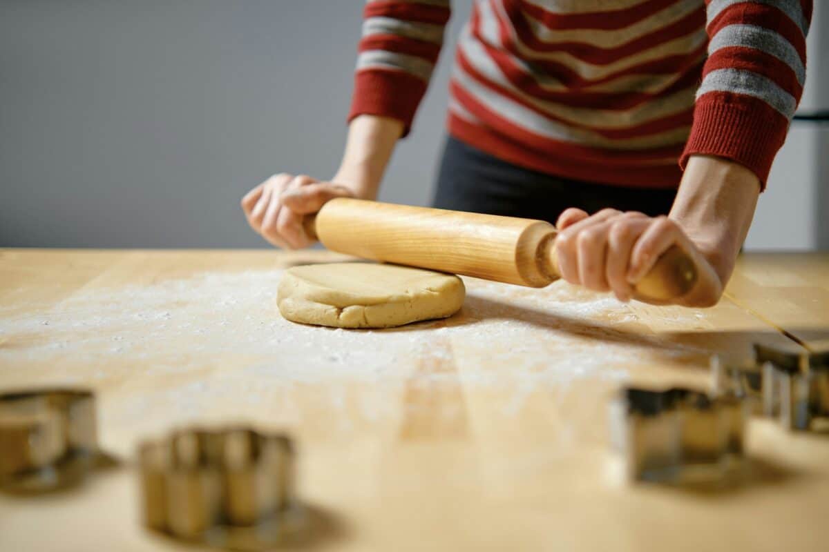 Une femme étale de la pâte de gingembre avec un rouleau à pâtisserie en bois dans la cuisine.