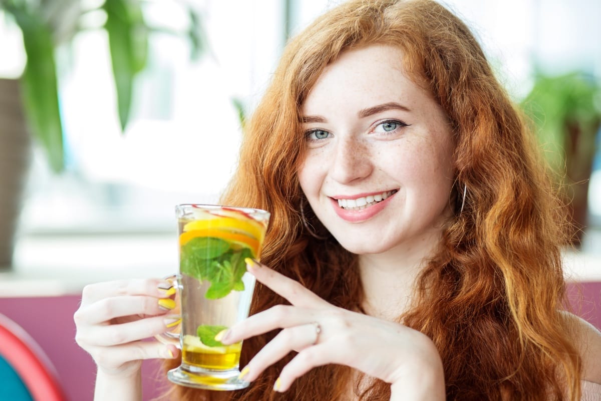 Une fille aux cheveux roux sourit. Thé à la menthe et aux agrumes. Concept de style de vie, de boissons et d'alimentation saine