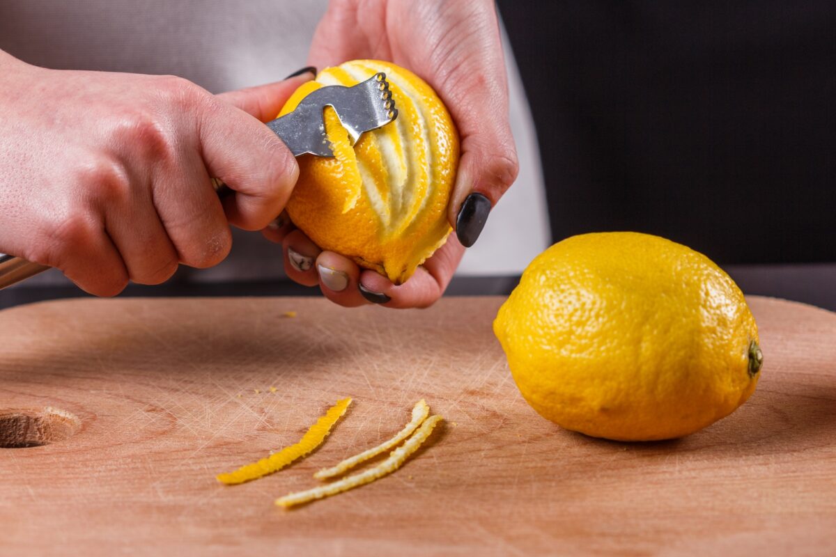 une jeune femme en tablier gris coupe des zestes de citron