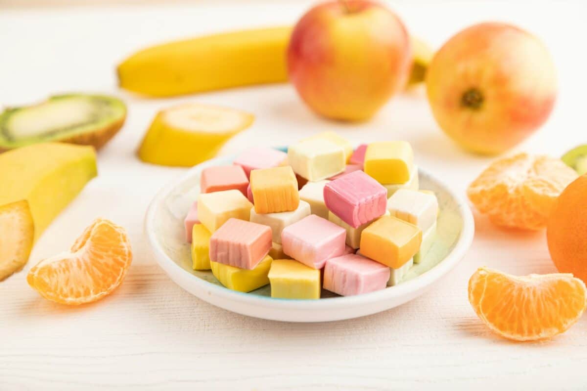 Various fruit jelly chewing candies on plate on white wooden background. apple, banana, tangerine
