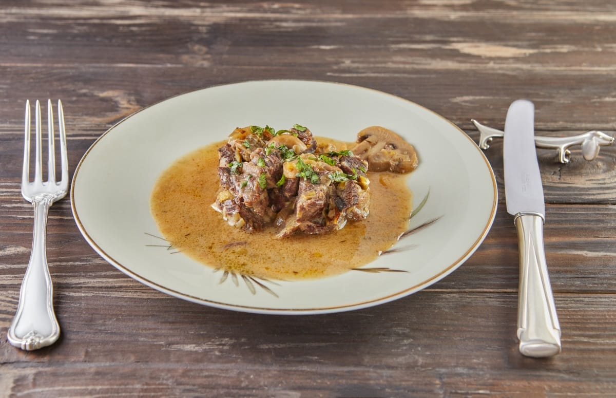 Veau braisé aux champignons dans des légumes verts dans une assiette sur fond de bois