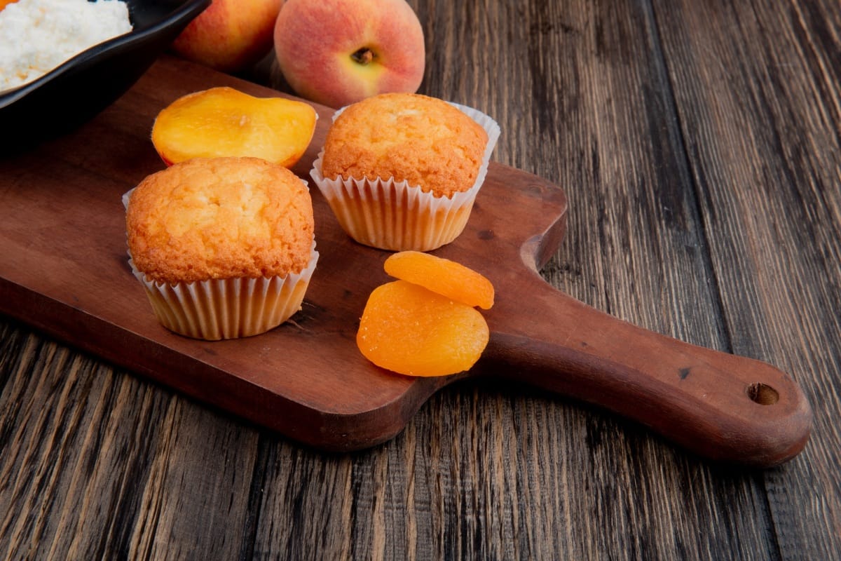 vue latérale de muffins avec abricots secs sur planche à découper en bois et pêches fraîches