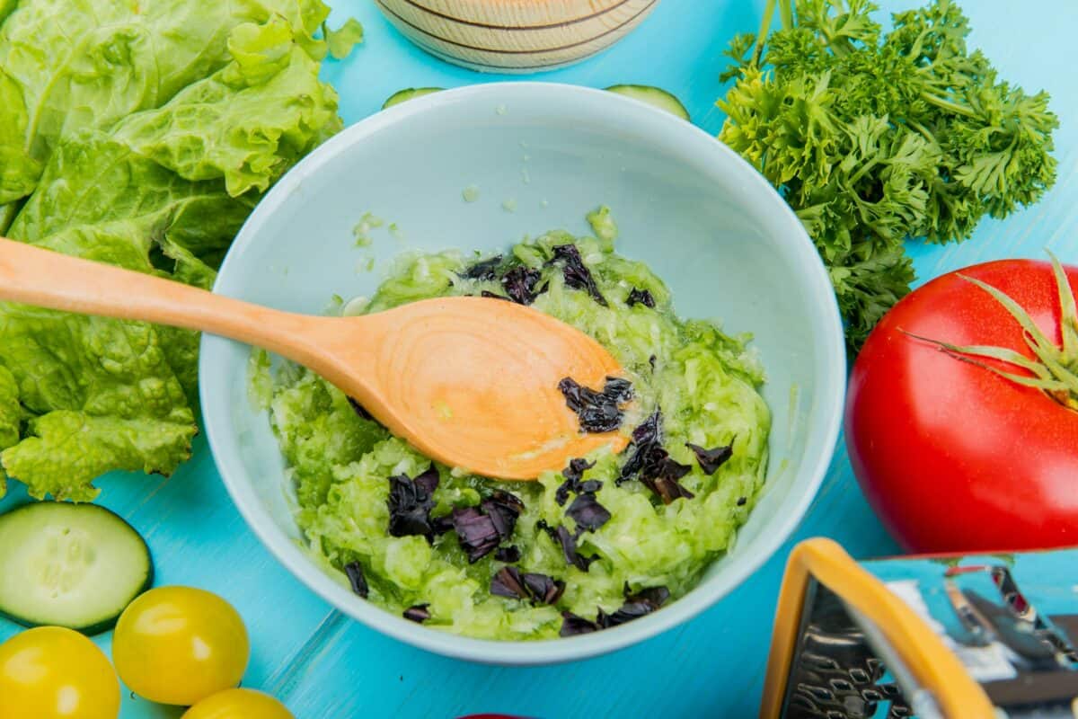 Vue rapprochée d'une salade de légumes avec laitue, concombre, tomate, coriandre et râpe en bois.