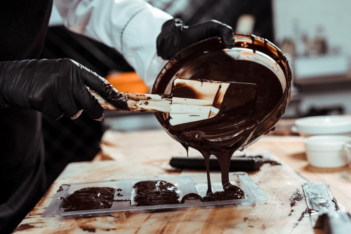 vue recadrée d'un chocolatier versant du chocolat fondu dans des moules à chocolat