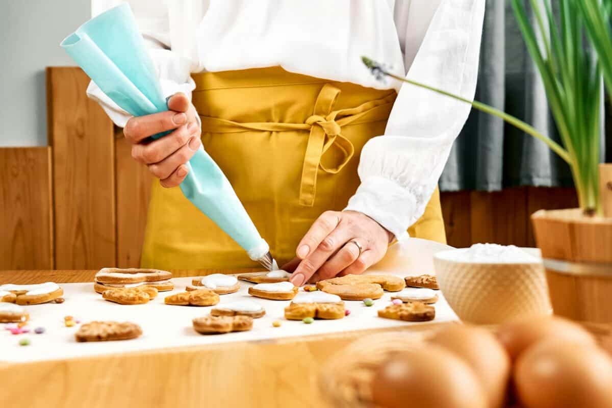 Woman decorating heart shaped cookies with frosting. Glazed festive homemade biscuits
