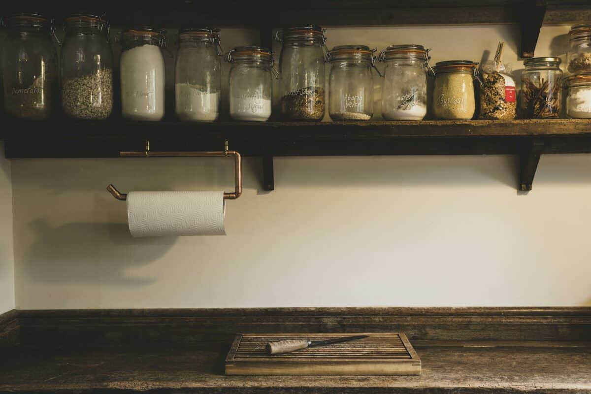 Wooden chopping board and knife on vintage wooden kitchen cupboard, row of glass jars with cooking