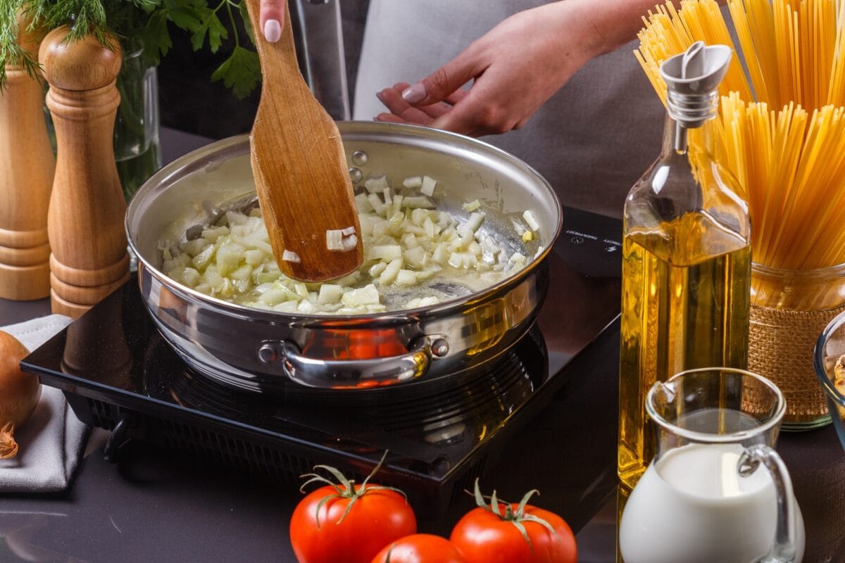 young woman in a gray apron roasts the onion in frying pan