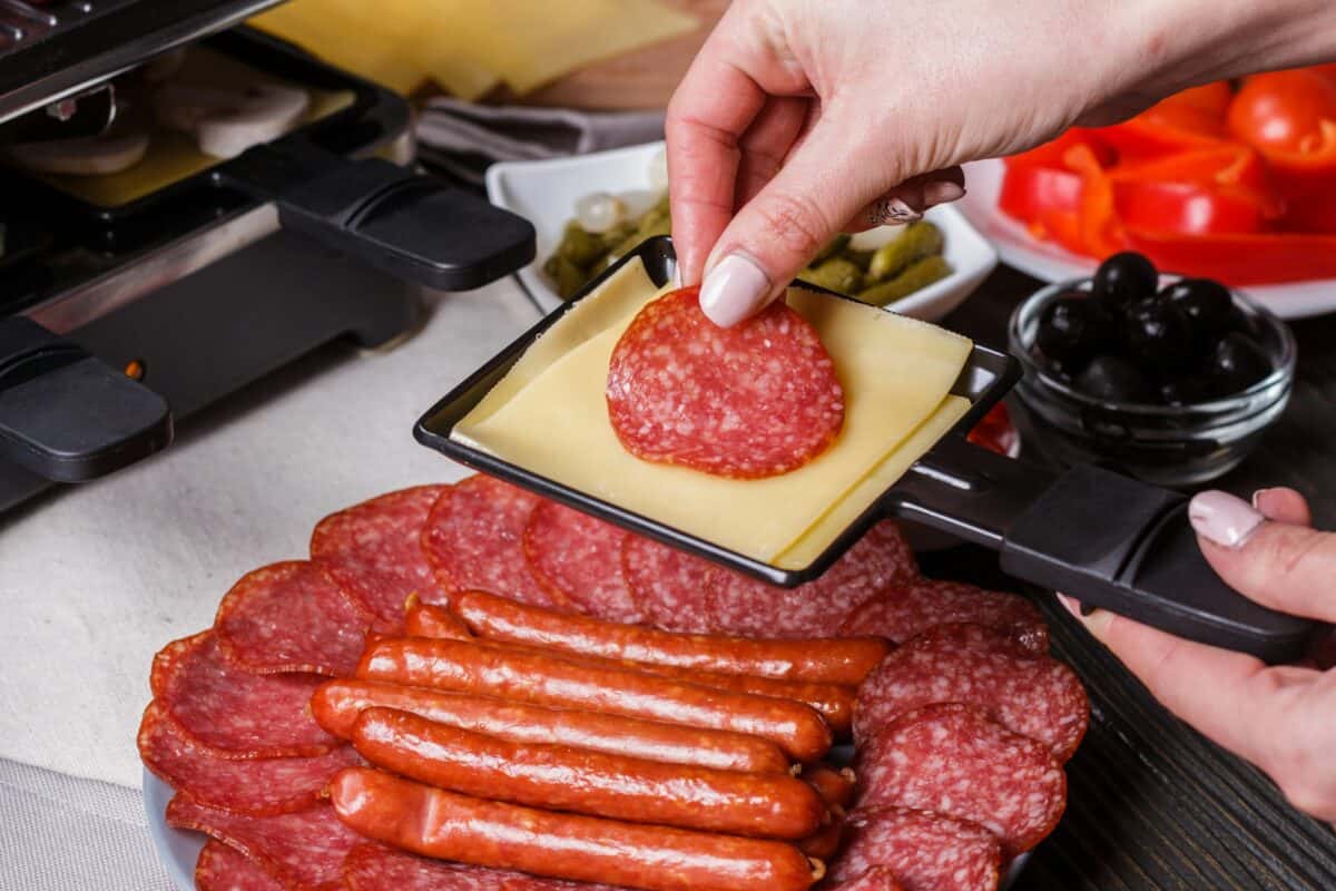 une jeune femme prépare une raclette traditionnelle au fromage suisse