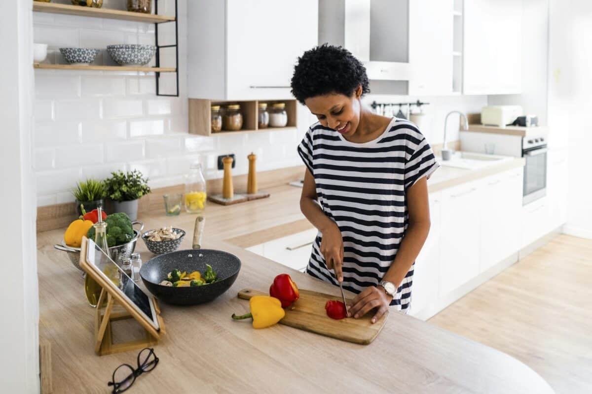 Young woman with tablet cooking in kitchen at home cutting vegetables